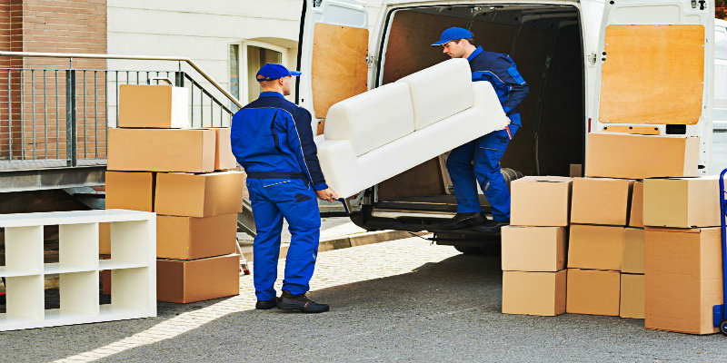 two men in blue uniform loading heavy furniture into the moving truck