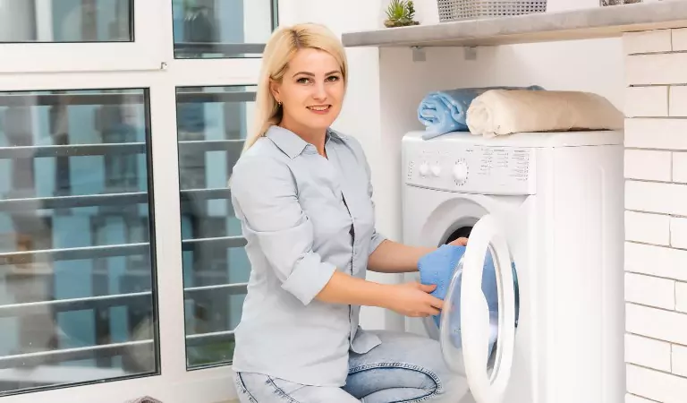 young woman putting clothes into a washing machine